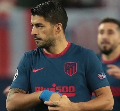 Luis Suarez is a famous professional football player who currently plays for Football Club Barcelona in the men’s top Spanish football division LaLiga Santander, commonly known as LaLiga. He is one of the best players today and is also one of the best strikers of his generation. Luis Suárez has achieved tremendous success and earned himself a lot of name and fame. He has 18 professional career trophies playing various events. Suarez is also infamously known for biting incidents on the pitch, but regardless, he is one of the best forwards the game has ever had. He is given El Pistolero, meaning ‘The Gunfighter’ because of his charismatic and bold personality and his ability to score goals from unusual distances and angles with the supervision of assisting his teammates. His jersey number is 9. Quick Info Full Name Luis Alberto Suarez Díaz Profession Football Player Birth Date January 24, 1987 Birth Place Salto, Uruguay Star Sign Aquarius Parents Father: Rodolfo Suarez Mother: Sandra Diaz Siblings 6 Wife Sofia Balbi Kids Delfina Suarez, Benjamin Suarez, Lautaro Suarez Net Worth $40 million Nationality Uruguayan Ethnicity Uruguayan Religion Roman Catholic Height 6 feet (1.82m/182cm) Weight 81kgs (179lbs) Eye Color Brown Hair Color Black Luis Suárez Bio Luis Suarez’s full name is Luis Alberto Suarez Díaz. He was born on 24 January 1987 to parents Rodolfo Suarez and Sandra Diaz in Salto, Uruguay. He was the fourth out of seven boys. Unfortunately, his parents split when he was just nine. One of his elder brothers, Paolo Suarez, is also a professional football player who used to play for Isidro Metapán, a Salvadoran football club based in El Salvador. Suarez had a tough childhood, spending most of it in poverty and also taking jobs of a sweeper when he was 15. Sadly, this later resulted in periodic aggression in the football field. He is currently 33 years old and has the zodiac sign of Aquarius. Nationality and Physical Stats Luis Suarez holds an Uruguayan nationality and is a Roman Catholic. He belongs to Uruguayan ethnicity. Besides this, he stands 6 feet (1.82m/182cm) tall and weighs around 81kgs (179lbs). He has a pair of brown-colored eyes with black hair color. Early Life Luis Suarez had a very tough childhood, as he spent most of it in poverty. His father walked away when he was nine, leaving Suarez with his mother and a large family to feed. His mother encouraged him to play football by letting him play for a famous football club called Urreta in Montevideo. The streets in Montevideo is where Suarez used to sweep alongside starting to develop his football skills. Not much is known about his education, but he is known to have never been so bright in his education. Later, he pursued a career in football when Wilson Perez spotted his potential while Suarez played for Urreta. As a teen, Suarez had a terrible company and used to drink. It was at the age of 15 when Suarez met his lifelong partner Sofia Balbi. According to Suarez, it was Sofia who helped him clear his head and made him realize how vital football was for him. He has also stated that Sofia helped him build a lot of confidence and belief in himself. Luis Suárez Career Early career-2007 Luis Suarez started his football career at seven when he moved to Montevideo and played for a youth club Urreta FC. He was spotted by Wilson Pirez. Wilson saw potential in young Suarez and signed him with the Nacional youth team at 14. Suarez made his debut with Nacional against Atlético Junior in the Copa Libertadores, an annual international club football competition organized by CONMEBOL since the 1960s. He started scoring goals from September 2005 and helped his team win the Uruguayan league in 2005-2006, scoring 10 goals with 27 appearances. During his time at Nacional, he became approached by scouts to buy him for a Dutch football club Groningen. He was transferred from Nacional to Groningen with a fee of €800,000. At the age of 19, Suarez left Nacional to play for Groningen. During his initial days in the team, he struggled to communicate as he could not speak Dutch or English. He started putting his efforts into learning the language and was respected by his teammates for doing so. Suarez began to blast the ball into the net but was notoriously aggressive. He used to score goals alongside being booked for disciplinary issues. After helping his team secure the eighth position in the 2006-2007 season of Eredivisie, he gained a proposal by Amsterdamsche Football Club Ajax or AFC Ajax, with a fee of €3.5 million. Suarez became upset when Groningen declined the offer. However, again Ajax offered €7.5 million for Suarez, which Groningen finally provided. 2007-Present In the 2007-2008 season, Suarez signed a five-year contract with Ajax. He scored a goal in his debut match for the team and helped Ajax finish in the second position. He scored 17 goals in 33 games and blended well with his teammate and league top scorer Klass-Jan Huntelaar. Suarez achieved his breakthrough moment when he ended the 2009-2010 season of Eredivisie as the top scorer of the league with 35 goals in 33 matches. He gained praise for his performance and named the Ajax Player of the Year. In a surprising turn of events, he bit PSV’s Otman Bakkal while fighting for the ball. For this notorious event, he became suspended for two matches and was also fined an undisclosed amount. Also, he gained the title as ‘Cannibal of Ajax’ by a Dutch daily, ‘De Telegraaf’. Suarez later uploaded a video apologizing for the misdemeanor. During his suspension, the Premier League giants Liverpool offered him a contract of €26.5 million. He left Ajax on good terms while still on suspension and started his career in the English Premier League as the most expensive transfer after Andy Carroll (€35 million). He signed a five-and-a-half-year contract with Liverpool on 31 January 2011. Luis Suarez, while playing for Liverpool, managed to nominate himself for the PFA Players’ Player of the Year. Also, he became the second top goal scorer of Liverpool and in the English Premier League in the 2012-2013 season with 23 goals. Also, he became Liverpool’s Player of the season in May 2013. Luis Suárez More In another surprising event, Suarez had his second biting incident, this time involving a Chelsea man Branislav Ivanovic. This led to him facing a series of problems starting with Ivanovic rejecting his apology and FA deciding a stiff penalty on the player with an undisposed fine. Even after facing harsh penalties, Suarez fought his way to the top when he became declared Player of the Year in 2013-2014. He scored twice and assisted once in the stunning 5-0 victory over Tottenham Hotspur. Following his brilliance, he managed to secure the top position in Europe’s Most Influential Player of the year. On 11 July 2014, Suarez signed a five-year contract with Spanish giants Barcelona for a whopping €82.3 million making him one of the most expensive players in the world of football. Since Suarez saw Gabriel Batistuta, Argentina number 9 as his idol, Barcelona made sure that Suarez wore the number 9 jersey. Suarez’s third biting incident became infamous when he bit Giorgio Chiellini in the 2014 FIFA World Cup. He missed training and participation with Barcelona during the first season as a punishment for the incident. Suarez made his competitive debut alongside teammates Lionel Messi and Neymar in the El Clasico match against Real Madrid but unfortunately lost the game. He ended his first season with Barcelona with an impressive record of 25 goals and 20 assists. Also, he partnered with Messi and Neymar forming a dominant attacking trio named ‘MSN’ after their initials. This trio absolutely dominated the league and managed to score a total of 122 goals, the most goals ever scored in a season by an attacking trio in the Spanish football history. The Italian football giants Juventus have shown interest in the Uruguayan, and Suarez has also agreed in advanced talks. Achievements Luis Suarez is known to be one of the gems of the modern football generation. He is a two-time Golden Boot Award winner. Also, he has a record of being the only player to win a Golden Boot with a Pichihci Trophy in the same year since 2009. He also has numerous Best Player awards to his name playing for significant teams in UEFA Champions League, LaLiga, and Eredivisie. Personal Life Luis Suarez has been together with Sofia Balbi since 15 and finally got married to her in 2009. This loving couple has a daughter Delfina Suarez in 2010, son Benjamin Suarez in 2013, and another son Lautaro Suarez in 2018. Social Luis Suarez is active on Instagram (@luissuarez9), with 38.2 million followers, and Twitter (@LuisSuarez9) with 16.2 million followers. He also has a verified Facebook page (@LuisSuarez9) with 18.1 million likes and 18.4 million followers. He has also launched a football complex ‘Complejo Suarez’ (complejosuarez.com) in Uruguay, which boasts indoor FIFA approved football pitches and outdoor barbeques. Net Worth Luis Suarez has struggled a lot during his childhood days and worked tirelessly to be recognized as one of the best footballers in the world today. He has certainly earned a tremendous amount of name and fame along with a handsome amount of money. As of 2020, Luis Suarez is worth $40 million.