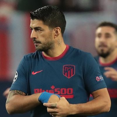 Luis Suarez is a famous professional football player who currently plays for Football Club Barcelona in the men’s top Spanish football division LaLiga Santander, commonly known as LaLiga. He is one of the best players today and is also one of the best strikers of his generation. Luis Suárez has achieved tremendous success and earned himself a lot of name and fame. He has 18 professional career trophies playing various events. Suarez is also infamously known for biting incidents on the pitch, but regardless, he is one of the best forwards the game has ever had. He is given El Pistolero, meaning ‘The Gunfighter’ because of his charismatic and bold personality and his ability to score goals from unusual distances and angles with the supervision of assisting his teammates. His jersey number is 9. Quick Info Full Name Luis Alberto Suarez Díaz Profession Football Player Birth Date January 24, 1987 Birth Place Salto, Uruguay Star Sign Aquarius Parents Father: Rodolfo Suarez Mother: Sandra Diaz Siblings 6 Wife Sofia Balbi Kids Delfina Suarez, Benjamin Suarez, Lautaro Suarez Net Worth $40 million Nationality Uruguayan Ethnicity Uruguayan Religion Roman Catholic Height 6 feet (1.82m/182cm) Weight 81kgs (179lbs) Eye Color Brown Hair Color Black Luis Suárez Bio Luis Suarez’s full name is Luis Alberto Suarez Díaz. He was born on 24 January 1987 to parents Rodolfo Suarez and Sandra Diaz in Salto, Uruguay. He was the fourth out of seven boys. Unfortunately, his parents split when he was just nine. One of his elder brothers, Paolo Suarez, is also a professional football player who used to play for Isidro Metapán, a Salvadoran football club based in El Salvador. Suarez had a tough childhood, spending most of it in poverty and also taking jobs of a sweeper when he was 15. Sadly, this later resulted in periodic aggression in the football field. He is currently 33 years old and has the zodiac sign of Aquarius. Nationality and Physical Stats Luis Suarez holds an Uruguayan nationality and is a Roman Catholic. He belongs to Uruguayan ethnicity. Besides this, he stands 6 feet (1.82m/182cm) tall and weighs around 81kgs (179lbs). He has a pair of brown-colored eyes with black hair color. Early Life Luis Suarez had a very tough childhood, as he spent most of it in poverty. His father walked away when he was nine, leaving Suarez with his mother and a large family to feed. His mother encouraged him to play football by letting him play for a famous football club called Urreta in Montevideo. The streets in Montevideo is where Suarez used to sweep alongside starting to develop his football skills. Not much is known about his education, but he is known to have never been so bright in his education. Later, he pursued a career in football when Wilson Perez spotted his potential while Suarez played for Urreta. As a teen, Suarez had a terrible company and used to drink. It was at the age of 15 when Suarez met his lifelong partner Sofia Balbi. According to Suarez, it was Sofia who helped him clear his head and made him realize how vital football was for him. He has also stated that Sofia helped him build a lot of confidence and belief in himself. Luis Suárez Career Early career-2007 Luis Suarez started his football career at seven when he moved to Montevideo and played for a youth club Urreta FC. He was spotted by Wilson Pirez. Wilson saw potential in young Suarez and signed him with the Nacional youth team at 14. Suarez made his debut with Nacional against Atlético Junior in the Copa Libertadores, an annual international club football competition organized by CONMEBOL since the 1960s. He started scoring goals from September 2005 and helped his team win the Uruguayan league in 2005-2006, scoring 10 goals with 27 appearances. During his time at Nacional, he became approached by scouts to buy him for a Dutch football club Groningen. He was transferred from Nacional to Groningen with a fee of €800,000. At the age of 19, Suarez left Nacional to play for Groningen. During his initial days in the team, he struggled to communicate as he could not speak Dutch or English. He started putting his efforts into learning the language and was respected by his teammates for doing so. Suarez began to blast the ball into the net but was notoriously aggressive. He used to score goals alongside being booked for disciplinary issues. After helping his team secure the eighth position in the 2006-2007 season of Eredivisie, he gained a proposal by Amsterdamsche Football Club Ajax or AFC Ajax, with a fee of €3.5 million. Suarez became upset when Groningen declined the offer. However, again Ajax offered €7.5 million for Suarez, which Groningen finally provided. 2007-Present In the 2007-2008 season, Suarez signed a five-year contract with Ajax. He scored a goal in his debut match for the team and helped Ajax finish in the second position. He scored 17 goals in 33 games and blended well with his teammate and league top scorer Klass-Jan Huntelaar. Suarez achieved his breakthrough moment when he ended the 2009-2010 season of Eredivisie as the top scorer of the league with 35 goals in 33 matches. He gained praise for his performance and named the Ajax Player of the Year. In a surprising turn of events, he bit PSV’s Otman Bakkal while fighting for the ball. For this notorious event, he became suspended for two matches and was also fined an undisclosed amount. Also, he gained the title as ‘Cannibal of Ajax’ by a Dutch daily, ‘De Telegraaf’. Suarez later uploaded a video apologizing for the misdemeanor. During his suspension, the Premier League giants Liverpool offered him a contract of €26.5 million. He left Ajax on good terms while still on suspension and started his career in the English Premier League as the most expensive transfer after Andy Carroll (€35 million). He signed a five-and-a-half-year contract with Liverpool on 31 January 2011. Luis Suarez, while playing for Liverpool, managed to nominate himself for the PFA Players’ Player of the Year. Also, he became the second top goal scorer of Liverpool and in the English Premier League in the 2012-2013 season with 23 goals. Also, he became Liverpool’s Player of the season in May 2013. Luis Suárez More In another surprising event, Suarez had his second biting incident, this time involving a Chelsea man Branislav Ivanovic. This led to him facing a series of problems starting with Ivanovic rejecting his apology and FA deciding a stiff penalty on the player with an undisposed fine. Even after facing harsh penalties, Suarez fought his way to the top when he became declared Player of the Year in 2013-2014. He scored twice and assisted once in the stunning 5-0 victory over Tottenham Hotspur. Following his brilliance, he managed to secure the top position in Europe’s Most Influential Player of the year. On 11 July 2014, Suarez signed a five-year contract with Spanish giants Barcelona for a whopping €82.3 million making him one of the most expensive players in the world of football. Since Suarez saw Gabriel Batistuta, Argentina number 9 as his idol, Barcelona made sure that Suarez wore the number 9 jersey. Suarez’s third biting incident became infamous when he bit Giorgio Chiellini in the 2014 FIFA World Cup. He missed training and participation with Barcelona during the first season as a punishment for the incident. Suarez made his competitive debut alongside teammates Lionel Messi and Neymar in the El Clasico match against Real Madrid but unfortunately lost the game. He ended his first season with Barcelona with an impressive record of 25 goals and 20 assists. Also, he partnered with Messi and Neymar forming a dominant attacking trio named ‘MSN’ after their initials. This trio absolutely dominated the league and managed to score a total of 122 goals, the most goals ever scored in a season by an attacking trio in the Spanish football history. The Italian football giants Juventus have shown interest in the Uruguayan, and Suarez has also agreed in advanced talks. Achievements Luis Suarez is known to be one of the gems of the modern football generation. He is a two-time Golden Boot Award winner. Also, he has a record of being the only player to win a Golden Boot with a Pichihci Trophy in the same year since 2009. He also has numerous Best Player awards to his name playing for significant teams in UEFA Champions League, LaLiga, and Eredivisie. Personal Life Luis Suarez has been together with Sofia Balbi since 15 and finally got married to her in 2009. This loving couple has a daughter Delfina Suarez in 2010, son Benjamin Suarez in 2013, and another son Lautaro Suarez in 2018. Social Luis Suarez is active on Instagram (@luissuarez9), with 38.2 million followers, and Twitter (@LuisSuarez9) with 16.2 million followers. He also has a verified Facebook page (@LuisSuarez9) with 18.1 million likes and 18.4 million followers. He has also launched a football complex ‘Complejo Suarez’ (complejosuarez.com) in Uruguay, which boasts indoor FIFA approved football pitches and outdoor barbeques. Net Worth Luis Suarez has struggled a lot during his childhood days and worked tirelessly to be recognized as one of the best footballers in the world today. He has certainly earned a tremendous amount of name and fame along with a handsome amount of money. As of 2020, Luis Suarez is worth $40 million.